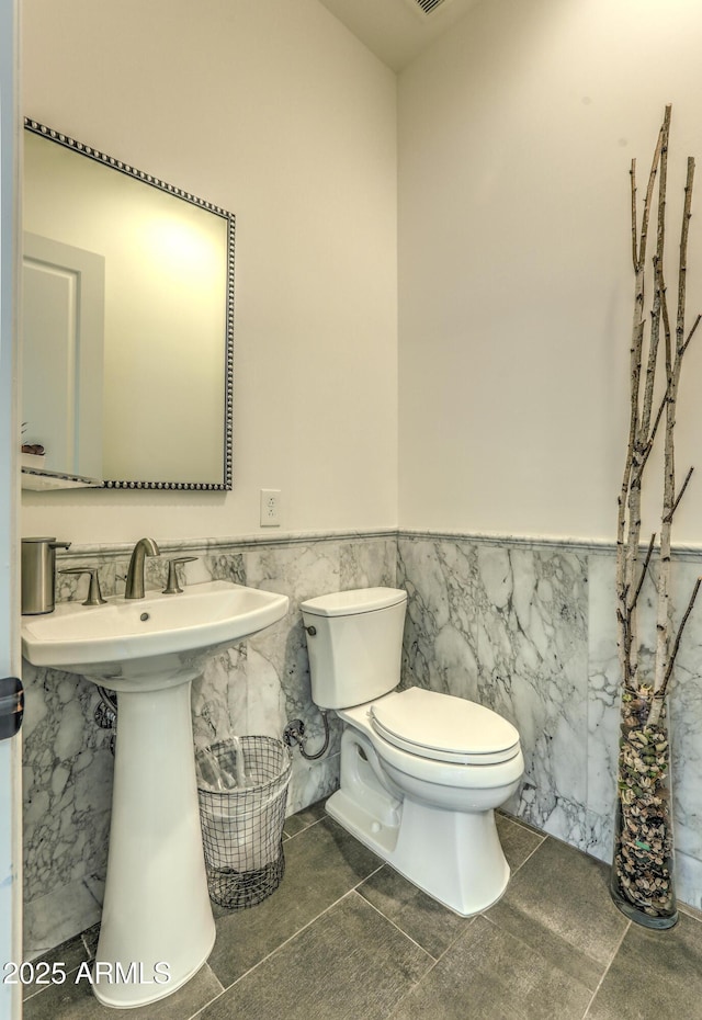 half bath featuring a wainscoted wall, a sink, tile walls, and toilet