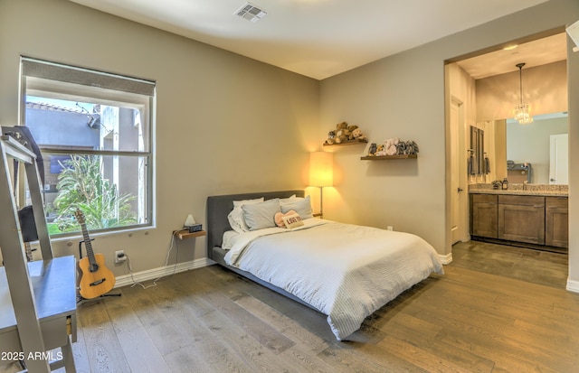 bedroom with hardwood / wood-style flooring, baseboards, visible vents, and connected bathroom