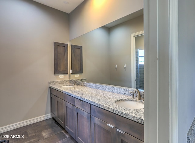 bathroom with double vanity, wood finish floors, a sink, and baseboards