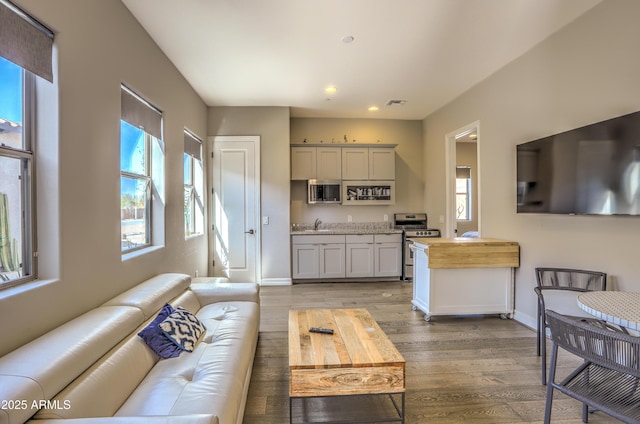 living room with light wood-style floors, visible vents, plenty of natural light, and baseboards