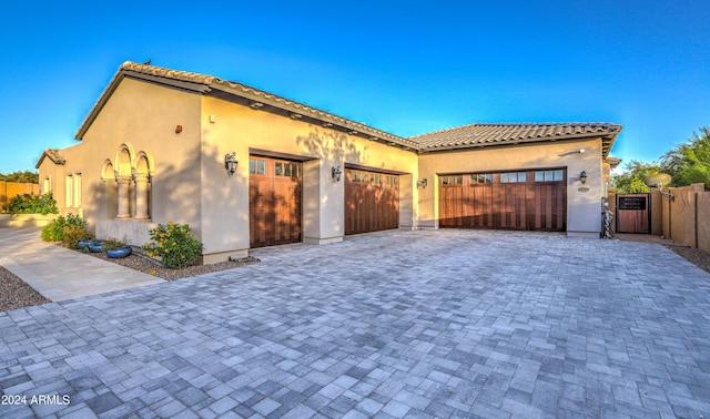 mediterranean / spanish house featuring decorative driveway, a tile roof, stucco siding, a gate, and a garage