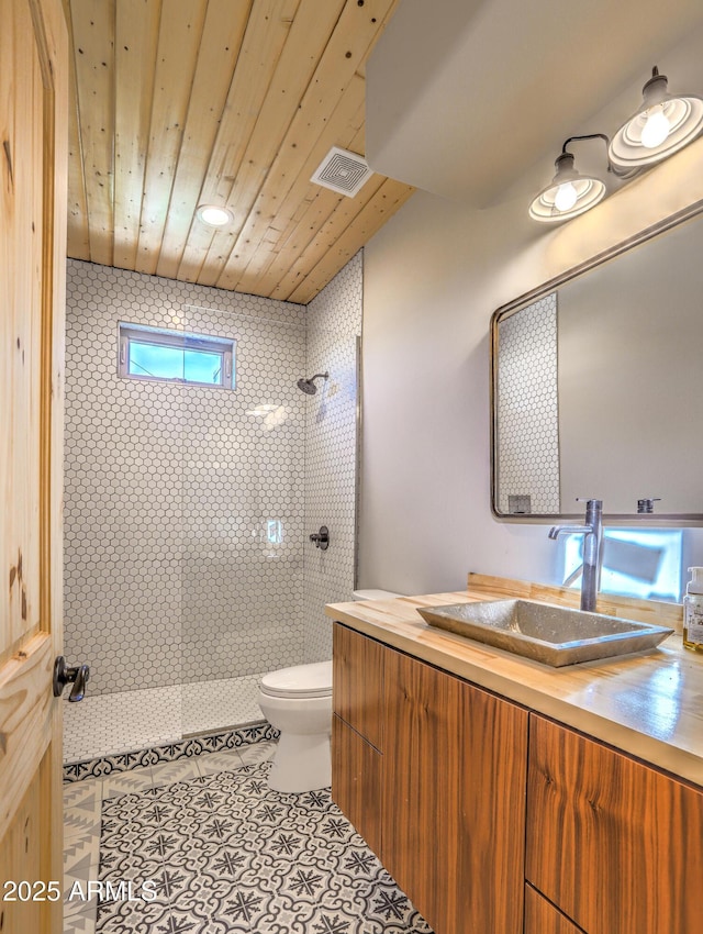 bathroom featuring toilet, visible vents, vanity, a tile shower, and tile patterned floors