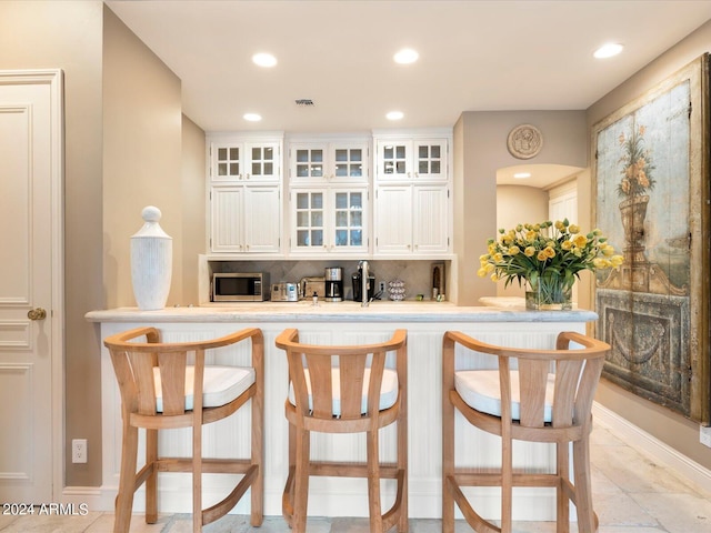 40 Biltmore Est, Phoenix, AZ 85016 - kitchen featuring tasteful backsplash, stainless steel microwave, a breakfast bar, light countertops, and white cabinetry