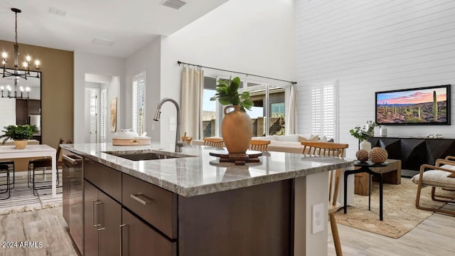 kitchen with decorative light fixtures, sink, dark brown cabinetry, light stone countertops, and a center island with sink