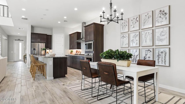 kitchen featuring a kitchen bar, a kitchen island with sink, light stone counters, stainless steel appliances, and wall chimney range hood