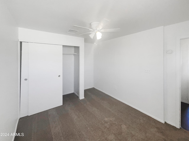 unfurnished bedroom with dark colored carpet, a closet, and ceiling fan