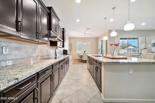 kitchen with black electric cooktop, an island with sink, hanging light fixtures, and backsplash