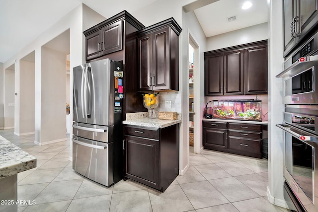 kitchen featuring stainless steel fridge, decorative backsplash, light tile patterned floors, light stone counters, and dark brown cabinetry