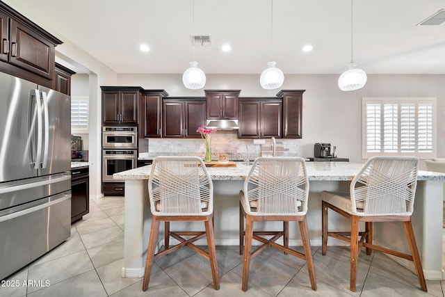 kitchen with a breakfast bar, appliances with stainless steel finishes, pendant lighting, light stone countertops, and decorative backsplash