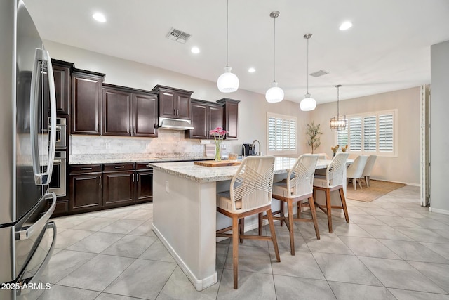 kitchen with a breakfast bar area, light stone counters, pendant lighting, stainless steel appliances, and a kitchen island with sink