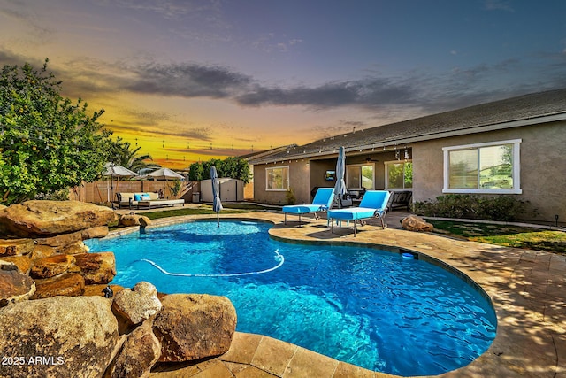 pool at dusk with a patio area and a shed