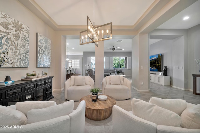 living room with ceiling fan with notable chandelier, light tile patterned floors, and a tray ceiling