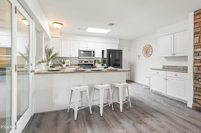 kitchen featuring light wood-type flooring, dark stone counters, appliances with stainless steel finishes, and white cabinetry