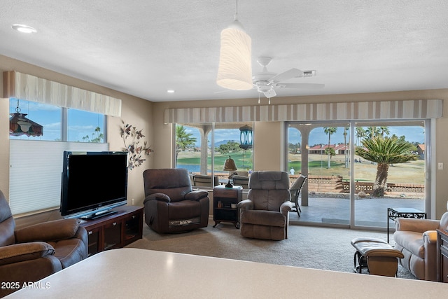 carpeted living room with a textured ceiling, ceiling fan, plenty of natural light, and visible vents