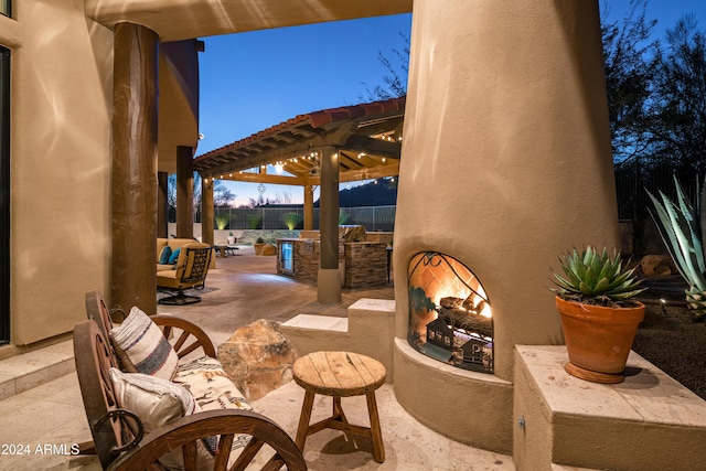 patio terrace at dusk with an outdoor fireplace, area for grilling, and a pergola