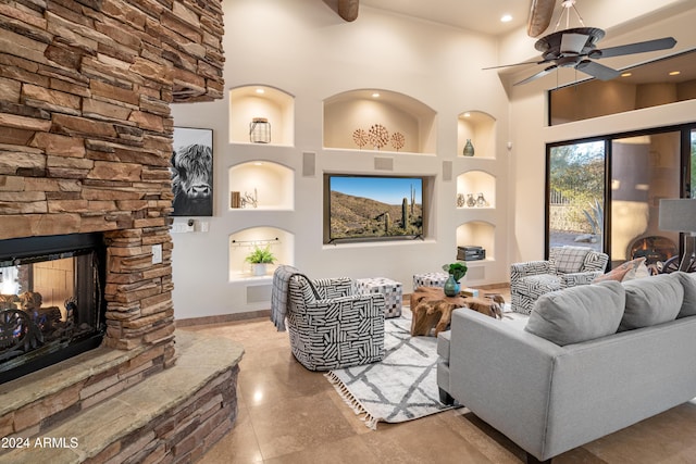 living room featuring ceiling fan, a high ceiling, built in shelves, and a fireplace