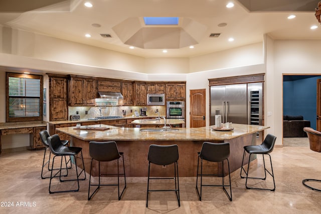 kitchen with a kitchen bar, built in appliances, a large island, and a towering ceiling