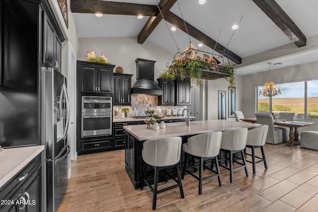 kitchen with a kitchen island with sink, a breakfast bar area, custom range hood, an inviting chandelier, and stainless steel appliances