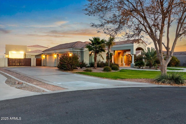 view of front of house featuring stucco siding, a lawn, fence, a garage, and driveway