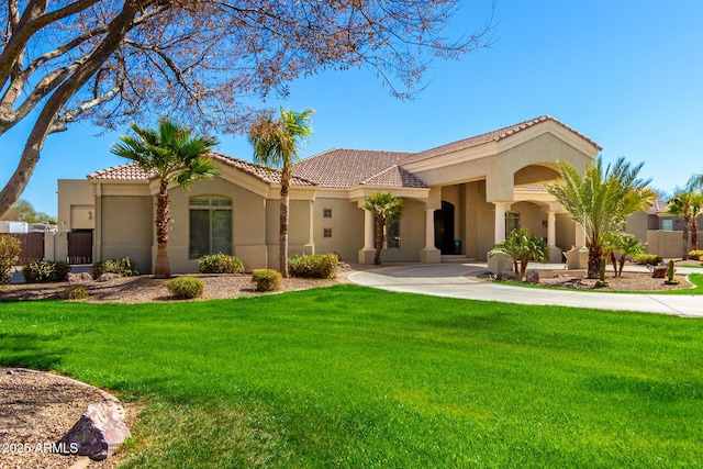 mediterranean / spanish-style home featuring a tiled roof, fence, a front lawn, and stucco siding