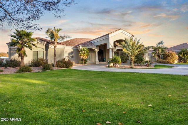 mediterranean / spanish home with driveway, a tiled roof, a front lawn, and stucco siding