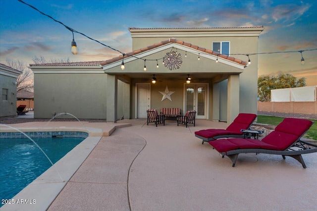 back of property at dusk featuring ceiling fan, a patio area, a fenced in pool, and stucco siding