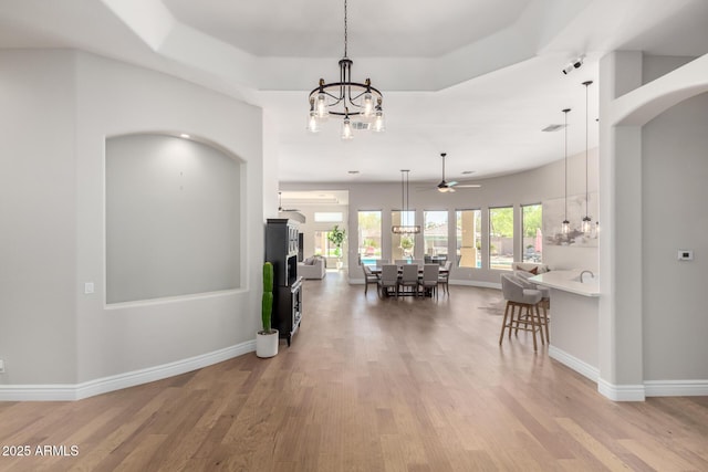 hall featuring arched walkways, a chandelier, baseboards, a tray ceiling, and light wood finished floors