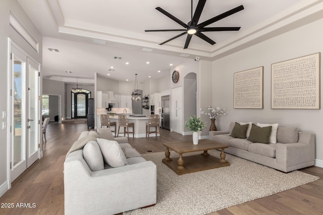 living area with visible vents, a tray ceiling, arched walkways, and wood finished floors