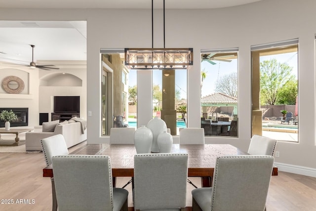 dining space featuring light wood-style flooring, baseboards, ceiling fan, and a glass covered fireplace