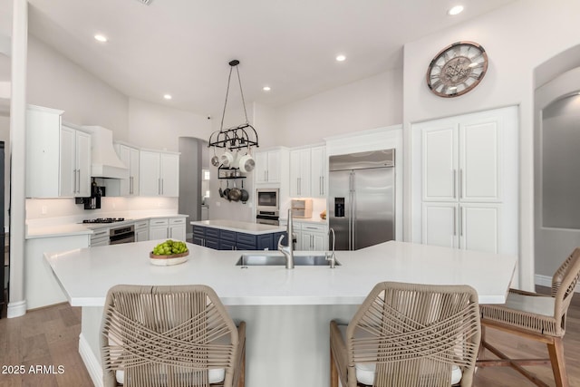 kitchen with custom exhaust hood, a spacious island, a sink, wood finished floors, and built in appliances