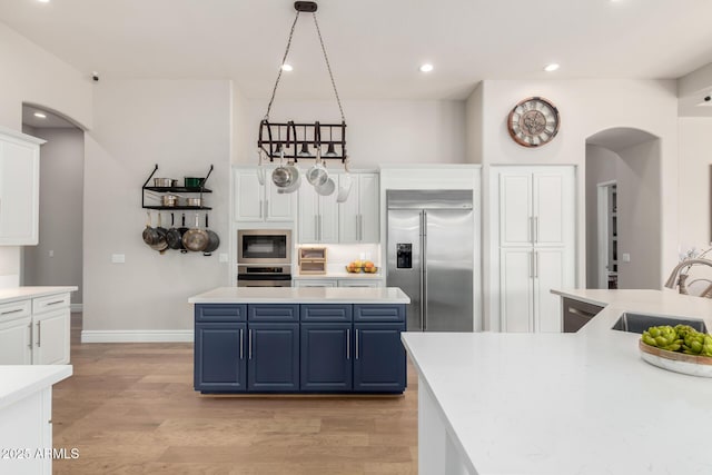 kitchen with arched walkways, a sink, blue cabinetry, and built in appliances