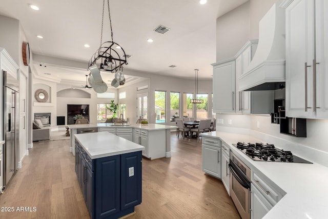 kitchen featuring a center island, blue cabinetry, stainless steel appliances, custom range hood, and open floor plan