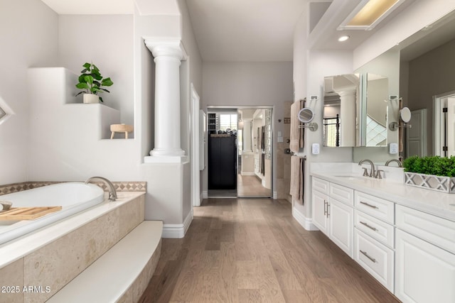 bathroom with a garden tub, wood finished floors, vanity, baseboards, and decorative columns