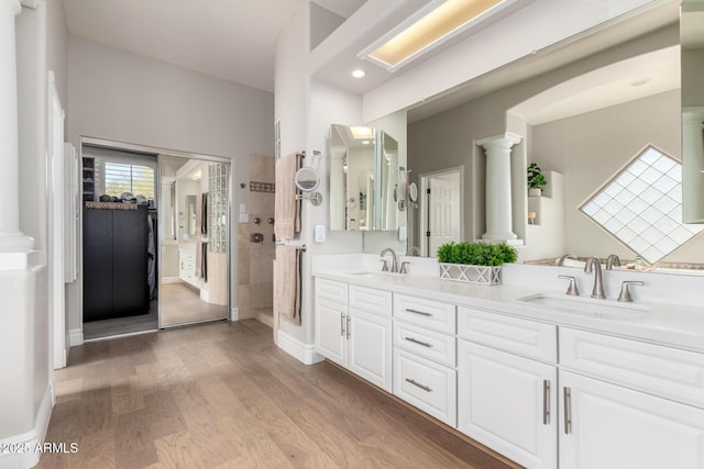 bathroom featuring a tile shower, wood finished floors, a sink, and ornate columns