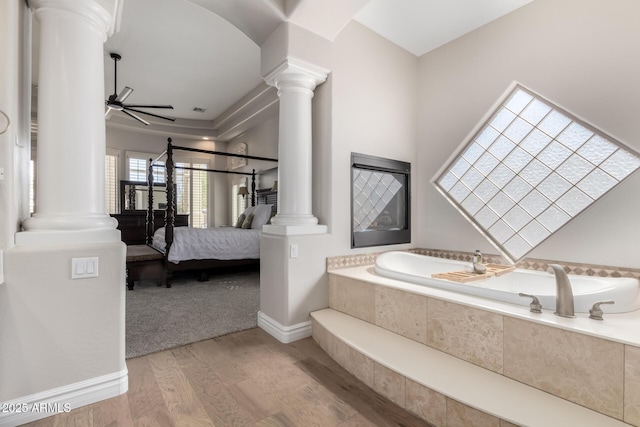 ensuite bathroom with ensuite bathroom, ceiling fan, a garden tub, wood finished floors, and ornate columns