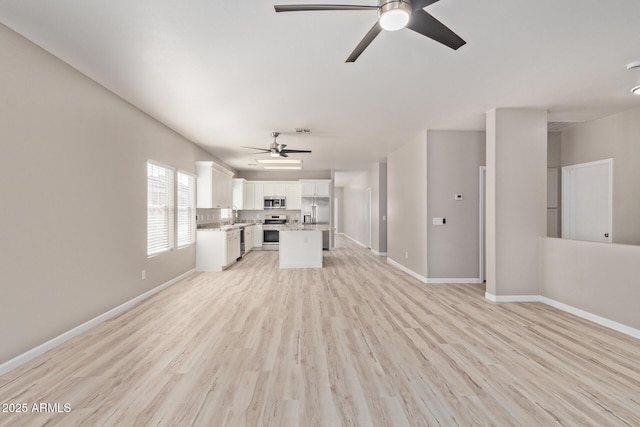 unfurnished living room featuring light wood-type flooring, a sink, a ceiling fan, and baseboards