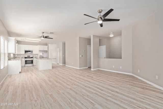 unfurnished living room with light wood-type flooring, ceiling fan, and baseboards