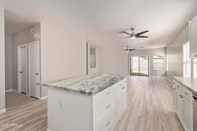 kitchen featuring light wood-type flooring, a kitchen island, light stone countertops, and white cabinets