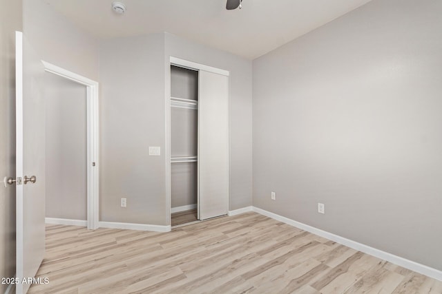 unfurnished bedroom with light wood-type flooring, a closet, ceiling fan, and baseboards