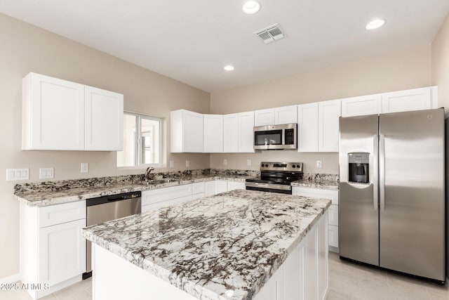 kitchen featuring light stone countertops, a kitchen island, white cabinetry, stainless steel appliances, and sink