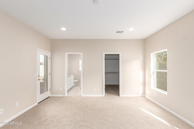 unfurnished bedroom featuring a closet, a walk in closet, light colored carpet, and ensuite bath