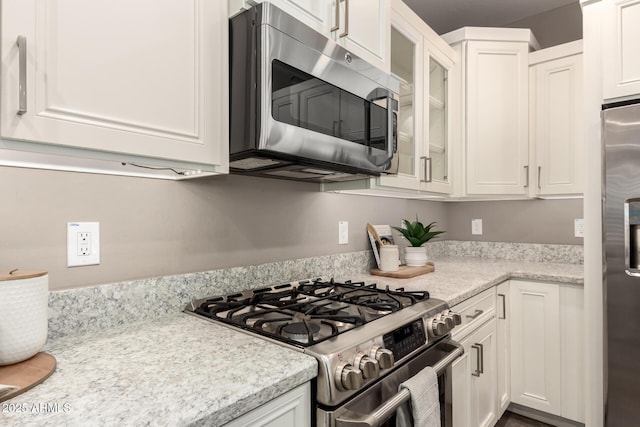 36145 N Desert Tea Dr, Queen Creek, AZ 85140 - kitchen with appliances with stainless steel finishes, white cabinetry, glass insert cabinets, and light stone countertops
