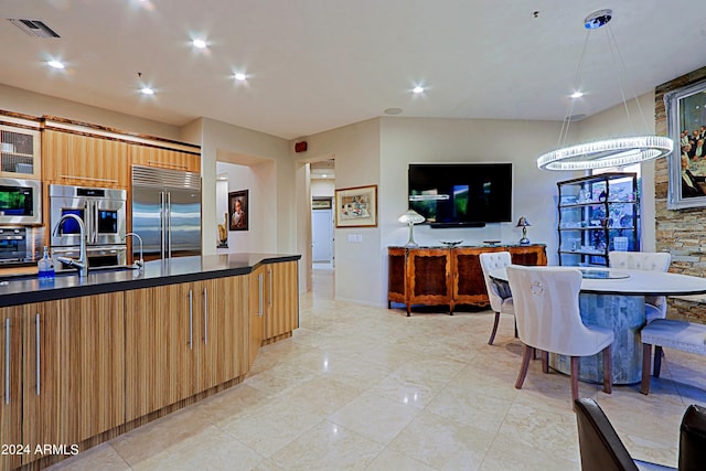 kitchen featuring sink, built in appliances, an island with sink, a chandelier, and decorative light fixtures