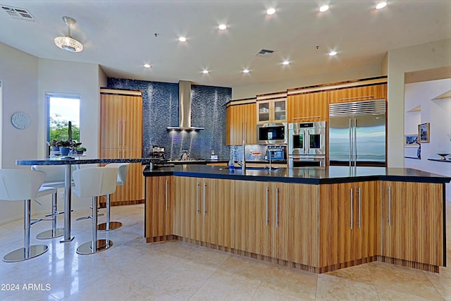 kitchen with decorative backsplash, stainless steel appliances, a spacious island, wall chimney range hood, and sink