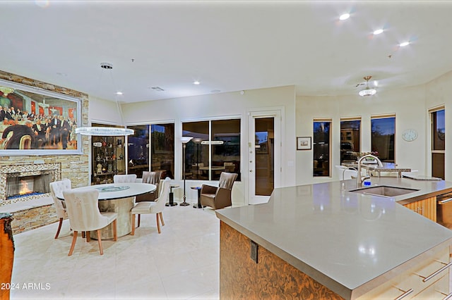 kitchen with pendant lighting, a stone fireplace, sink, an island with sink, and light tile patterned flooring