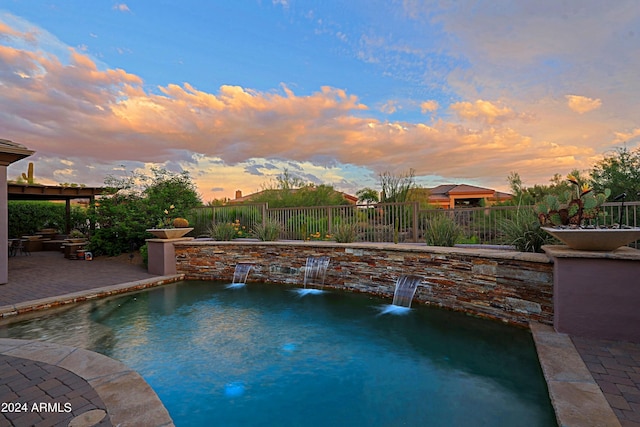 pool at dusk with pool water feature and a patio