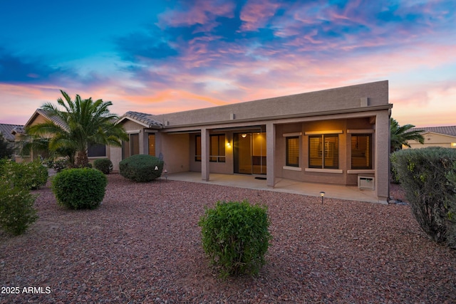 back of property at dusk featuring stucco siding and a patio area
