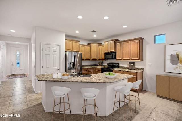 kitchen featuring visible vents, a center island with sink, a sink, and black appliances