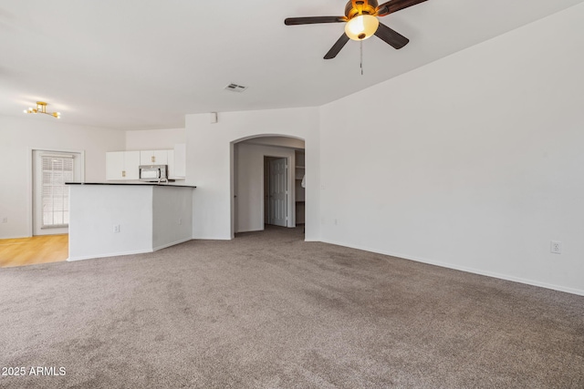 unfurnished living room with visible vents, arched walkways, light carpet, and ceiling fan