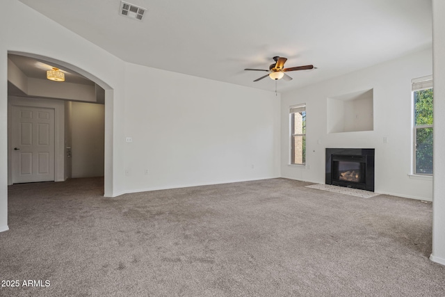 unfurnished living room featuring a wealth of natural light, visible vents, carpet floors, and a ceiling fan